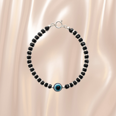 Black beaded bracelet with a blue evil eye charm on a beige fabric background
