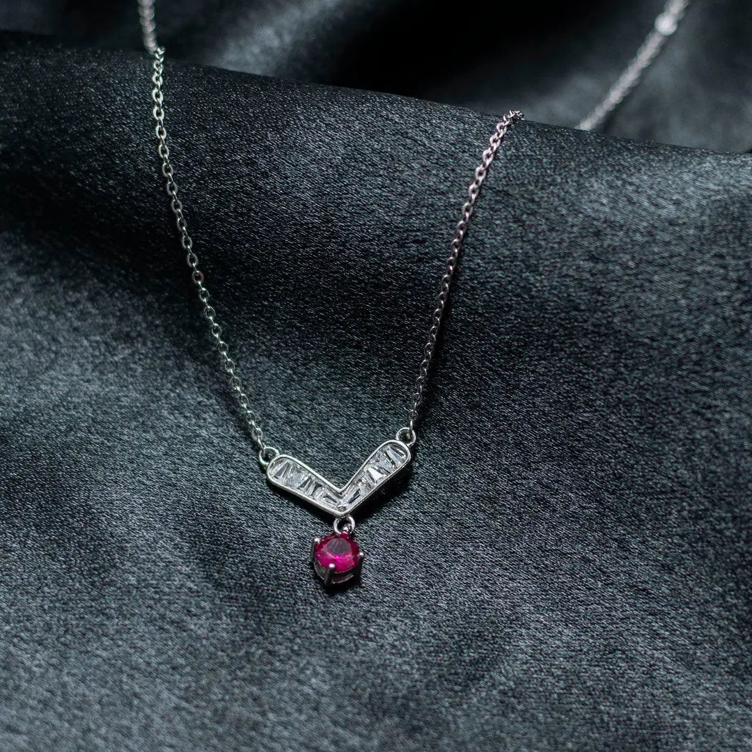Silver necklace with a red gemstone pendant on a dark fabric background