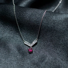 Silver necklace with a red gemstone pendant on a dark fabric background