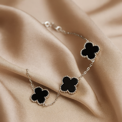 Silver bracelet with black clover-shaped charms on beige fabric