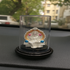 Silver deity figure in a glass display case on a car dashboard with blurred background