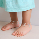 Children's feet wearing silver heart-shaped anklets on a neutral background