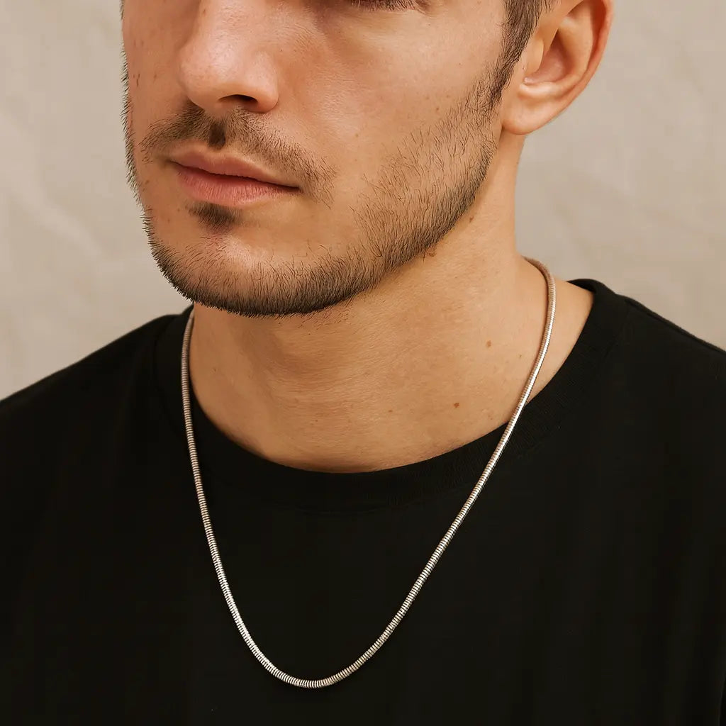 Man wearing a silver chain necklace against a neutral background