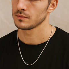 Man wearing a silver chain necklace against a neutral background