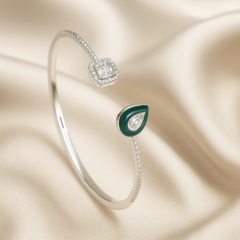 Silver bracelet with green teardrop charm on a beige satin background