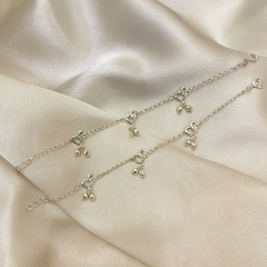 Silver bracelet with heart and bell charms on a beige fabric background