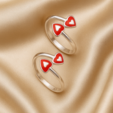 Two gold rings with red heart-shaped designs on a beige fabric background