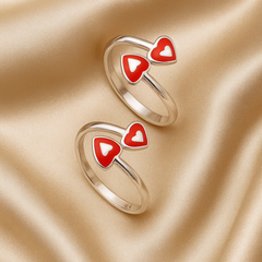 Two gold rings with red heart-shaped designs on a beige fabric background