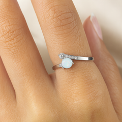 Silver ring with a gemstone on a person's finger against a neutral background
