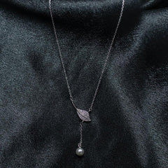 Necklace with leaf and pearl pendant on a dark fabric background
