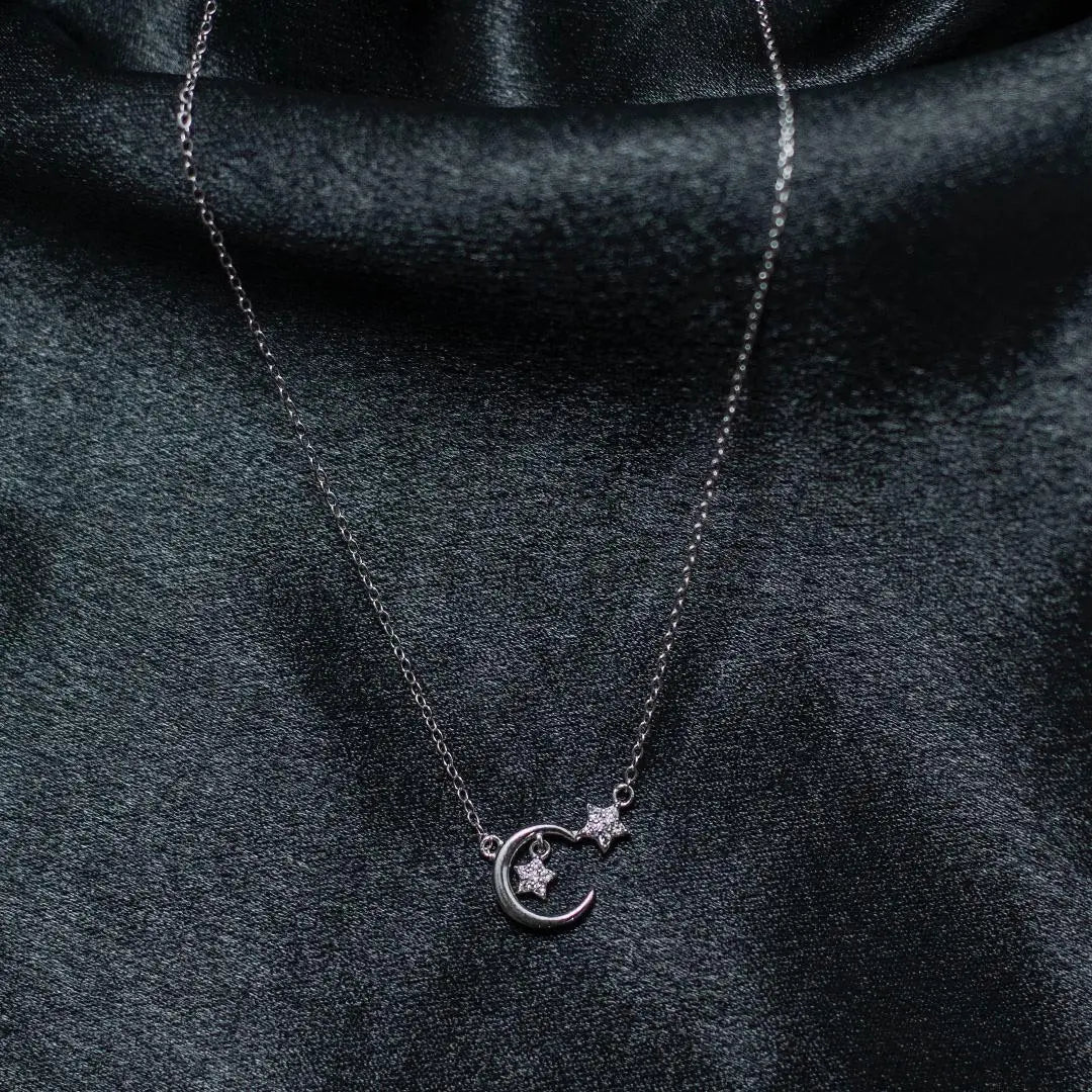 Silver necklace with a moon and star pendant on a dark fabric background