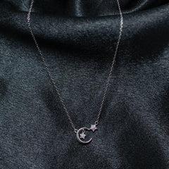 Silver necklace with a moon and star pendant on a dark fabric background