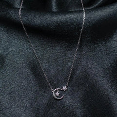 Silver necklace with a moon and star pendant on a dark fabric background