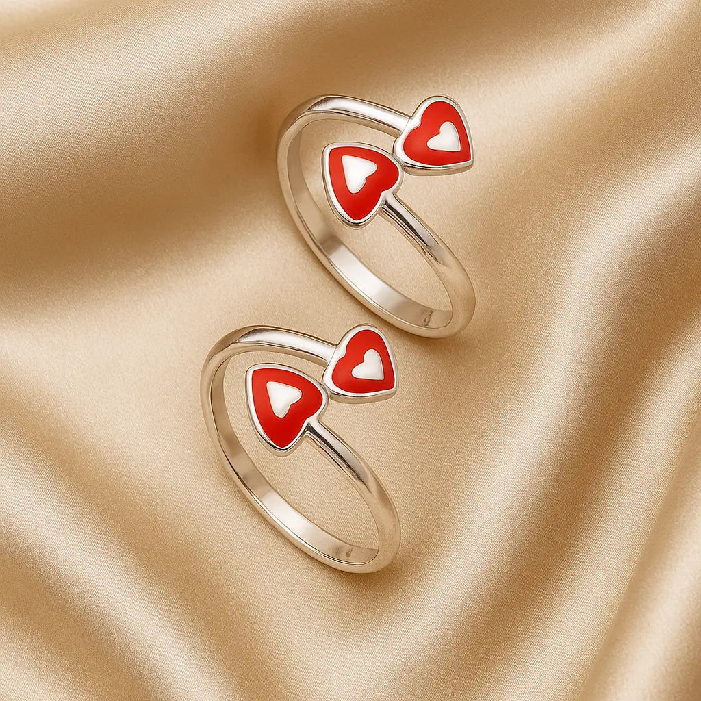 Two gold rings with red heart-shaped designs on a beige fabric background