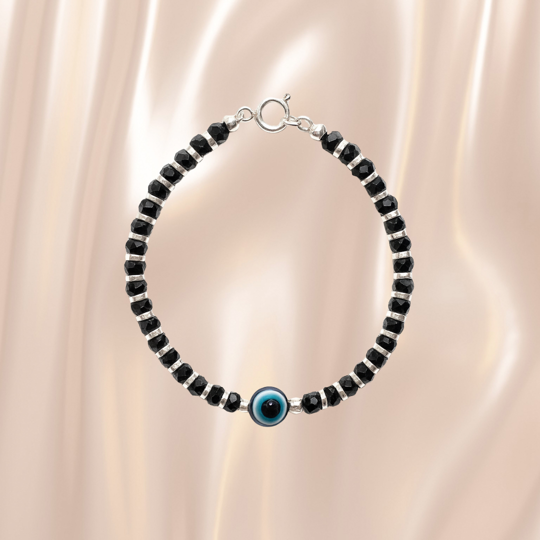 Black beaded bracelet with a blue evil eye charm on a beige fabric background