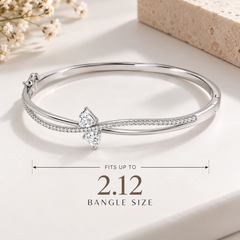 A silver-toned hinged bangle bracelet featuring a bow-shaped setting with two clear heart-cut gemstones and a row of small pavé-set stones along the curved upper band, shown on a white background.