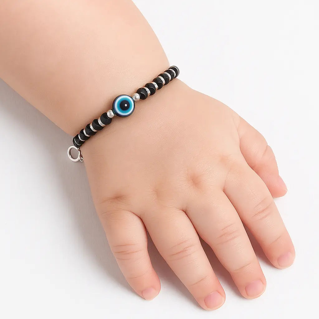 Hand wearing a black and white beaded bracelet with a blue evil eye charm on a light background