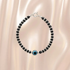 Black beaded bracelet with a blue evil eye charm on a beige fabric background