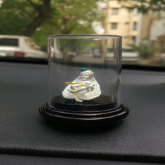 Silver figurine in a transparent glass dome on a car dashboard with blurred background