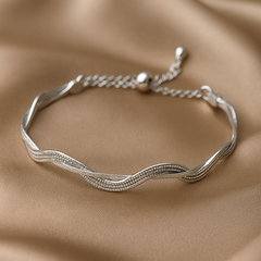 Silver bracelet with wavy design on a beige fabric background