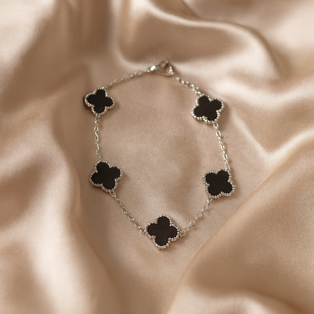 Silver bracelet with black clover-shaped charms on a beige fabric background