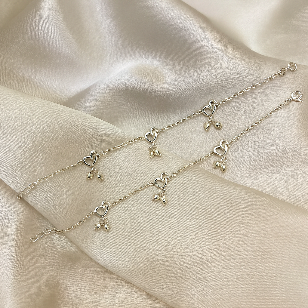 Silver bracelet with heart and bell charms on a beige fabric background