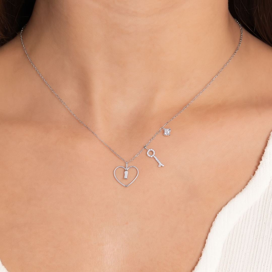 Silver necklace with heart, key, and round pendant on a model wearing a white top.