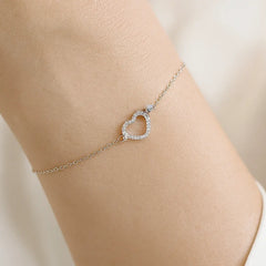 Silver anklet with a heart-shaped clasp on a person's ankle against a neutral background