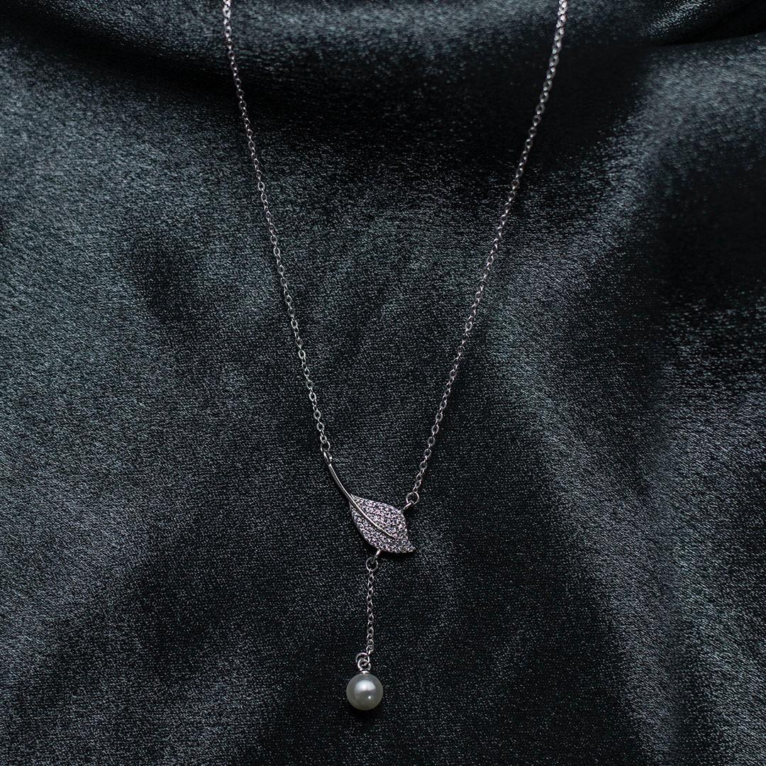 Necklace with leaf and pearl pendant on a dark fabric background