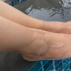 Close-up of a person's ankle with a gold anklet by a pool.