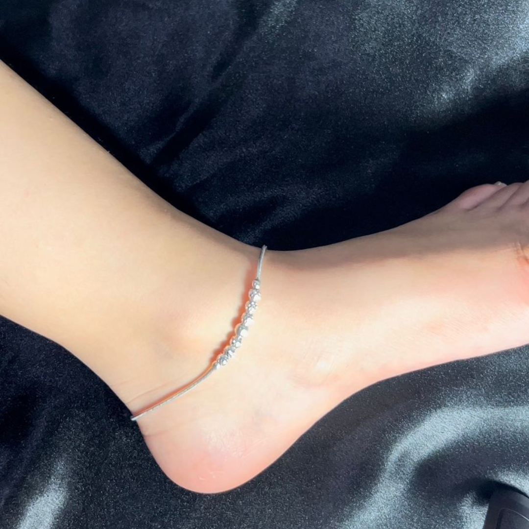 Silver anklet on a person's ankle against a dark fabric background