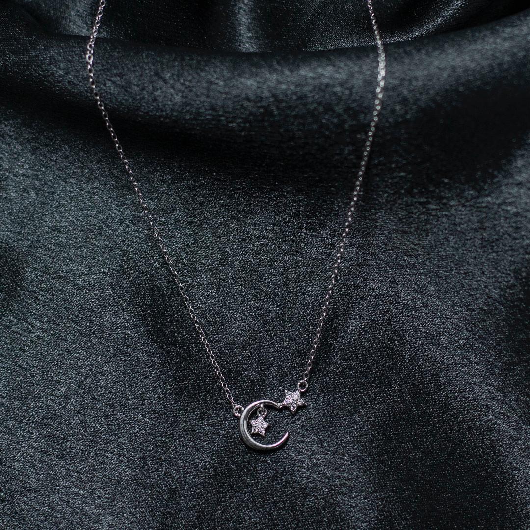 Silver necklace with a moon and star pendant on a dark fabric background