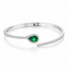 A polished silver-toned open cuff bracelet with a teardrop-shaped green gemstone surrounded by small clear stones, displayed on a soft cream fabric background with a textured block and text reading 'FITS UP TO WRIST 2.8'.